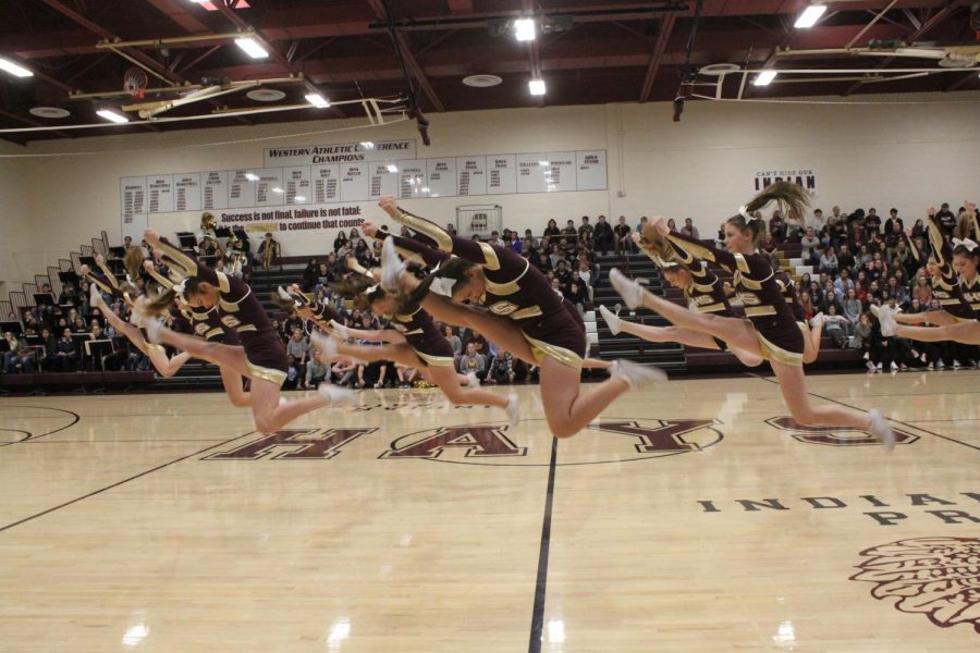 The cheerleaders perform jumps together.