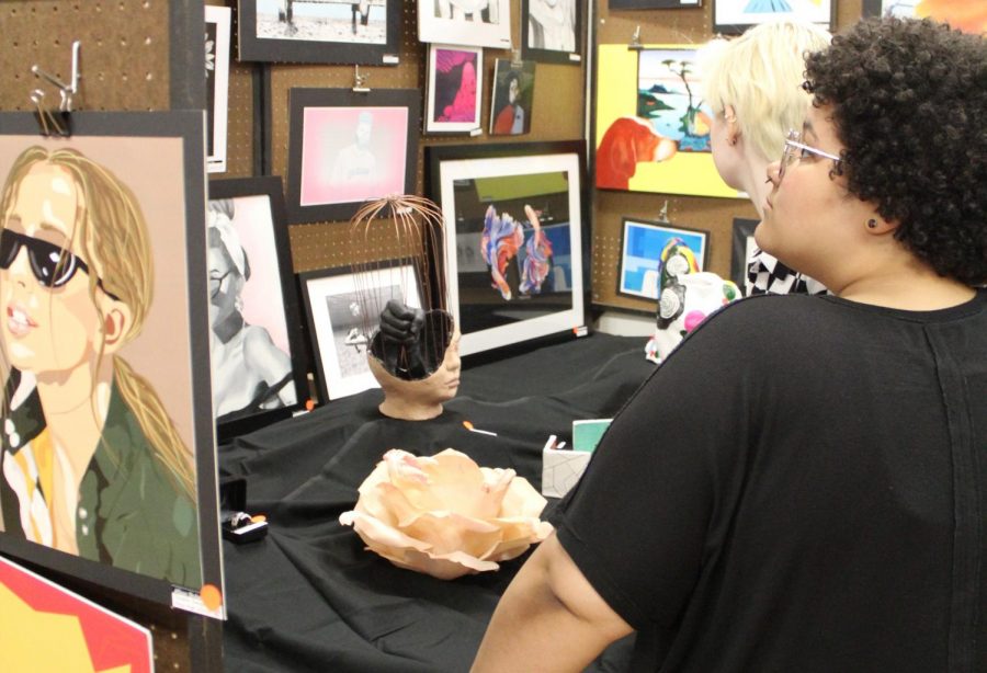 Seniors Mollie Hoar and Taysia McCoy view the work displayed in a booth from one of the attending schools. Many art students contributed to the Hays High School art booth.