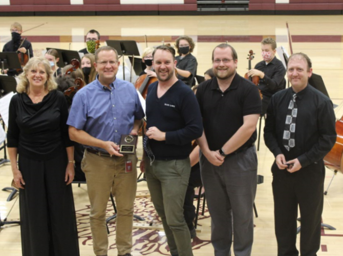 Orchestra director Joan Crull, principal Martin Straub, vocal director Alex Underwood, band director Matthew Rome and assistant orchestra director Nathan Mark pose in front of the Concert Orchestra after awarding Straub with his KMEA Honor Administrator of the Year plaque at the Fall Orchestra Concert that was held on Oct. 13 in Gym A.