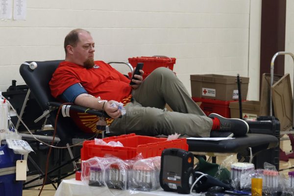 Science teacher Thomas Decker checks out his phone while giving blood at the HOSA spring blood drive on May 9.
