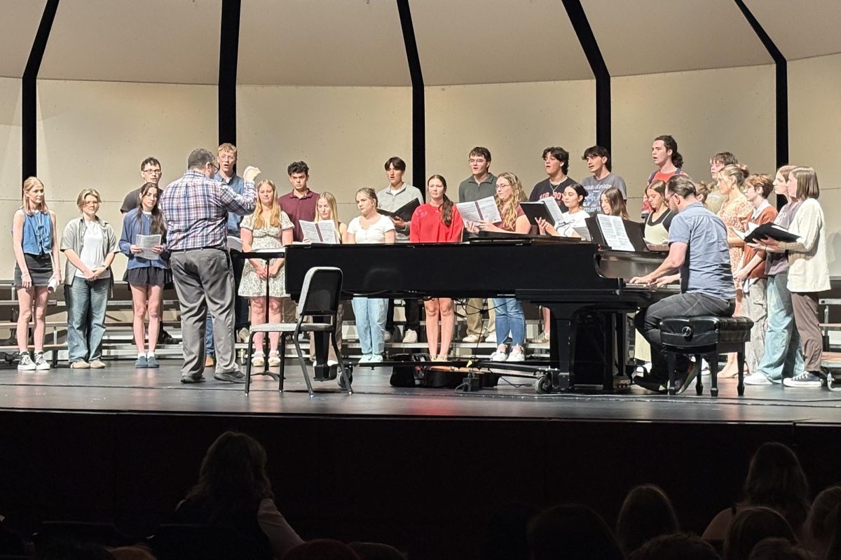 Chamber Singers sing together in harmony, as director Micheal Davidson leads and director Alex Underwood accompanies them on piano on stage. 