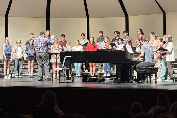 Chamber Singers sing together in harmony, as director Micheal Davidson leads and director Alex Underwood accompanies them on piano on stage. 